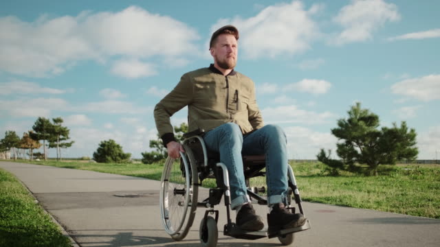 Männlicher-Patient-im-Rollstuhl-geht-bei-warmem-Wetter-im-Park