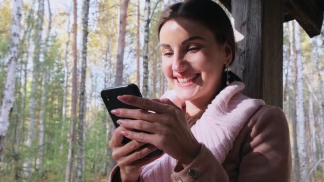 Happy-attractive-woman,-in-the-autumn-spring-forest,-communicates-on-social-networks-via-phone