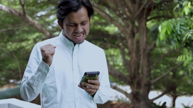 Hombre-emocionado-asiático-disfrutar-del-éxito-mientras-se-utiliza-Smartphone