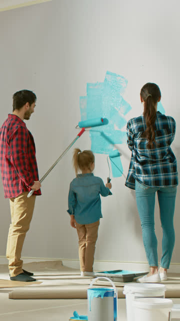 Back-Shot-of-a-Family-Painting-Walls-with-Their-Cute-Small-Daughter.-They-Paint-with-Rollers-that-are-Covered-in-Light-Blue-Paint.-Room-Renovations.Video-Footage-with-Vertical-Screen-Orientation-9:16