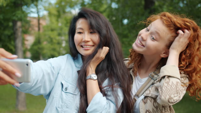 Attraktive-junge-Frauen-machen-Selfie-im-Freien-im-Park-berührende-Haare-lächelnd