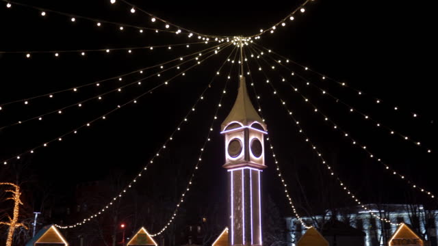 Torre-del-reloj-decorada-con-luces-de-Navidad,-guirnaldas-de-bombillas-en-el-mercado-de-Año-Nuevo-de-la-plaza-de-la-ciudad.-La-cámara-vuela-alrededor-del-Big-Ben-decorativo-en-Nochebuena.-Conceptos-de-tiempo-y-vacaciones