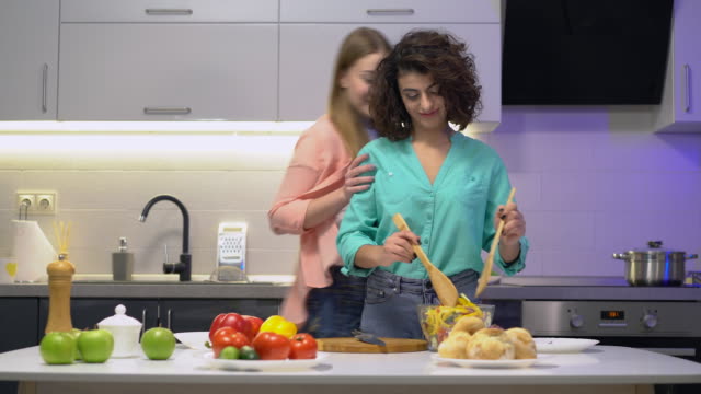 Lesbian-couple-tasting-salad-in-kitchen,-spending-time-together,-relationship