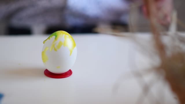 El-niño-litlle-con-un-pincel-pinta-un-huevo-de-Pascua-en-color-amarillo-en-un-soporte-sobre-la-mesa.