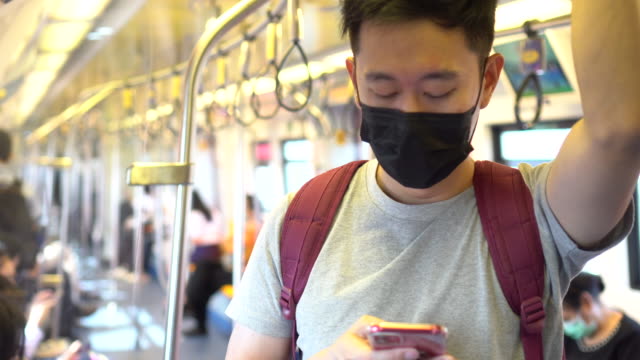 Nahaufnahme-eines-jungen-asiatischen-Mannes-trägt-eine-schwarze-chirurgische-Gesichtsmaske-und-mit-einem-Handy-in-der-U-Bahn-Zug-während-der-neuen-Typ-Coronavirus-Covid-19-Lungenentzündung-Ausbruch-und-pm-2.5-Smog-Luftverschmutzung-Krise-in-der-Großsta
