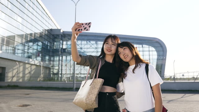 Slow-motion-of-exuberant-cute-asian-female-mates-making-selfie-on-the-airport-background