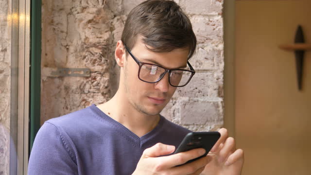 Young-man-in-glasses-holds-smartphone-and-reads-information