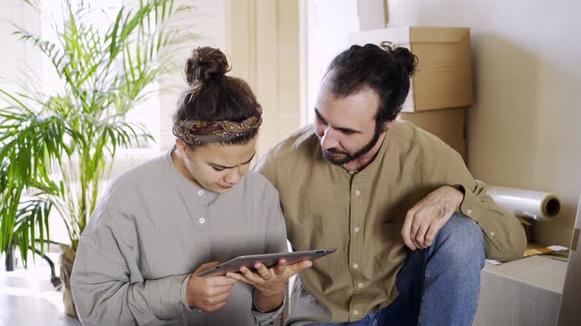 Couple-using-tablet-in-new-flat-near-pile-of-boxes
