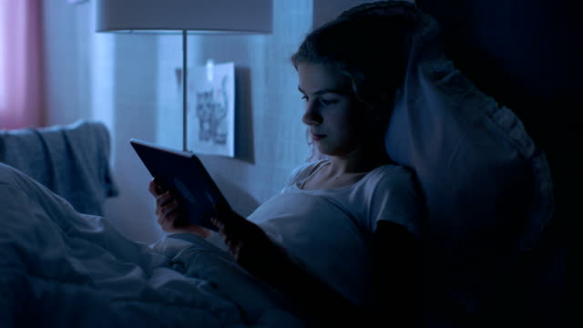 Joven-adolescente-se-encuentra-en-su-cama-en-la-noche-con-Tablet-Computer.-Relojes-TV-Show.