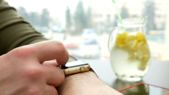 Closeup-view-of-man-checking-for-notifications-on-smartwatch-while-sitting-at-table-with-lemonade-pitche