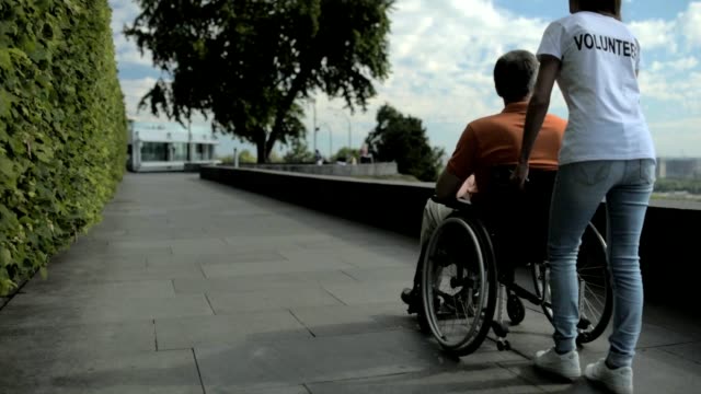 Vista-posterior-de-un-voluntariado-femenino-caminando-con-un-hombre-wheelchaired