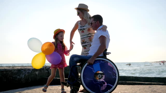 happy-family,-Disabled-in-wheelchair-stroll-with-pregnant-wife,-child-holds-air-balloons-and-jumping,-invalid-with-wife