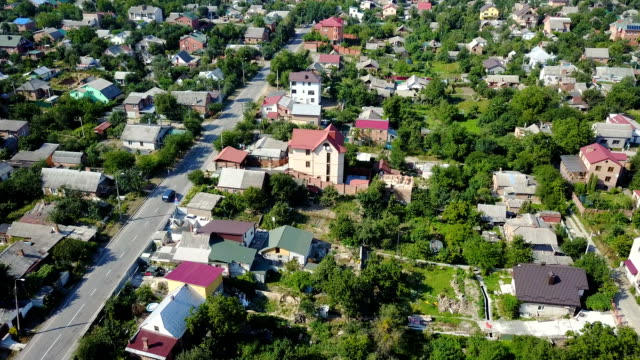 Video-from-the-drone.-View-from-high-to-a-car-that-rides-along-an-asphalt-road-in-a-small-suburban-village.-The-camera-moves-down-above-the-roofs-of-houses.