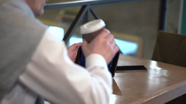 Reife-Geschäftsmann-überwacht-Handel-Kryptowährung-auf-Tablet-und-trinken-Kaffee-in-einem-café
