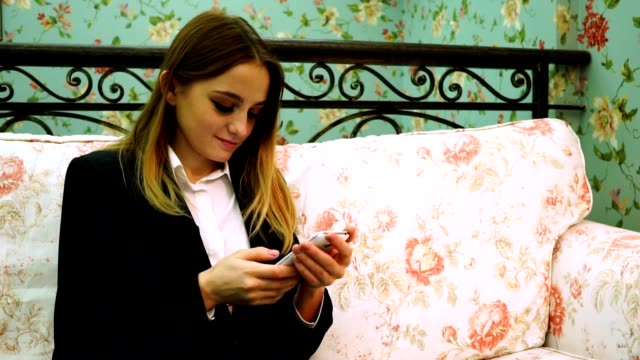 Girl-in-a-white-shirt-and-jacket-typing-on-a-smartphone-sitting-on-the-couch