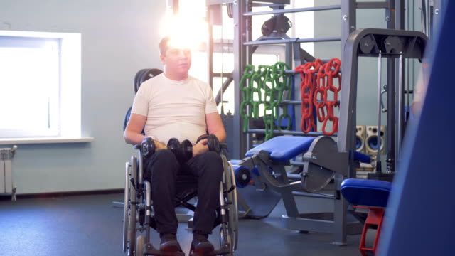 Ein-behinderter-Mann-im-Rollstuhl-sitzt-in-der-Mitte-ein-Fitness-Studio,-sprechen-und-Lächeln