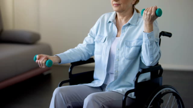 Mujer-anciana-en-silla-de-ruedas-levantar-pesas-en-el-centro-de-rehabilitación,-trauma