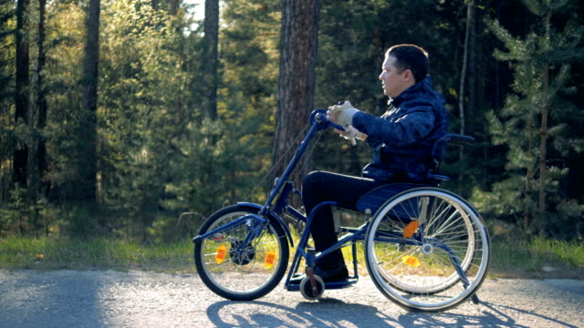 Un-hombre-con-discapacidad-va-en-una-silla-de-ruedas-en-un-camino-forestal,-vista-lateral.