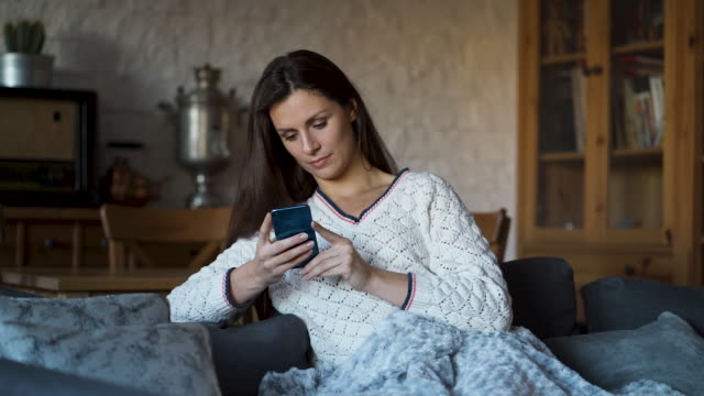 woman-sitting-on-the-couch-wrapped-in-a-blanket-and-texting-on-the-phone