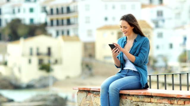 Happy-woman-browsing-on-phone-on-a-ledge