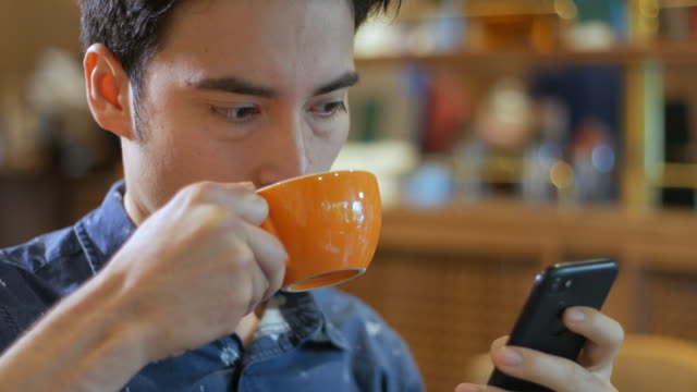 Attractive-hispanic-Latin-American-man-holding-smartphone-and-drinking-coffee-in-a-coffee-shop,-close-up
