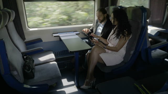 Young-corporate-couple-man-and-woman-discussing-about-business-project-using-their-device-tablet-pc-and-smartphone-while-they-traveling-by-train