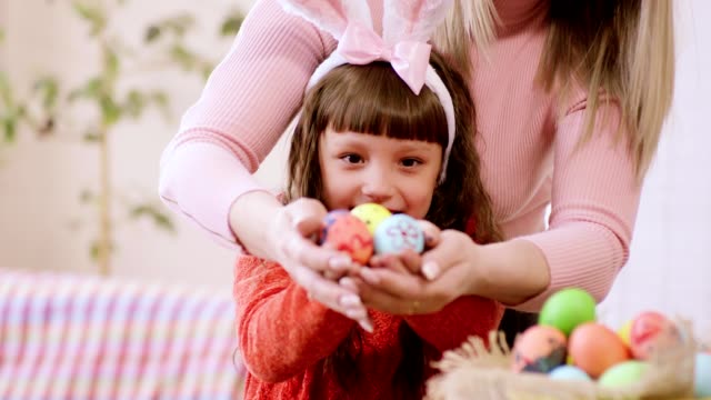 mamá-y-su-hija-están-sonriendo-ampliamente,-sosteniendo-sus-manos-con-huevos-de-Pascua-a-la-cámara.