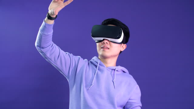 Asiatischer-junger-Mann,-der-Virtual-Reality-Headset-verwendet,-isoliert-über-violetten-Hintergrund