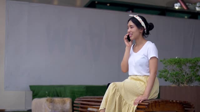 Retrato-joven-mujer-asiática-sentada-hablando-en-el-teléfono-sonriendo-y-la-felicidad.-Hermoso-estilo-de-vida-de-negocios-joven-usando-tecnología.