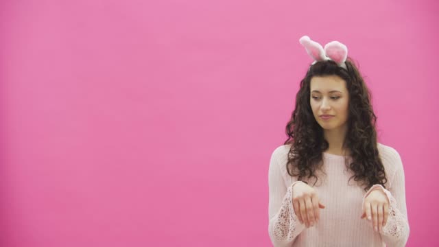 Young-beautiful-couple-standing-on-a-pink-background.-During-this-they-make-movements-of-rabbits.-The-woman-put-her-hands-on-her-neck.-Gentle-views-and-touches-to-each-other.-On-the-head-rabbit-ears.