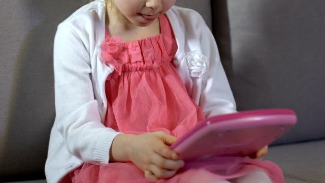 Niño-femenino-jugando-juguete-de-la-tableta-del-sofá-sentado,-ocio-de-la-infancia,-juguete-educativo