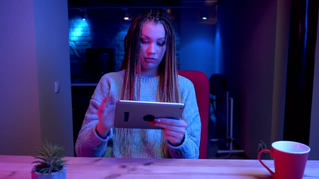 Closeup-shoot-of-young-attractive-female-blogger-with-dreadlocks-playing-video-gameson-the-tablet-winning-and-being-happy-streaming-live-with-the-neon-background-indoors