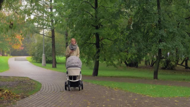 Frau-mit-Handy-beim-Gehen-mit-Baby-im-Herbstpark