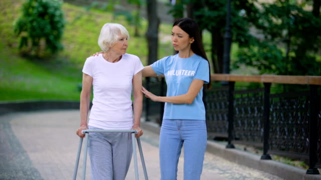 Female-volunteer-supporting-sick-old-woman-walking-frame,-rehab-difficulties