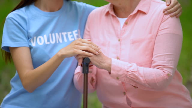 Sozialfreiwilliger-streichelt-alte-Patientin-Hand-auf-Gehstock,-Hospizhilfe