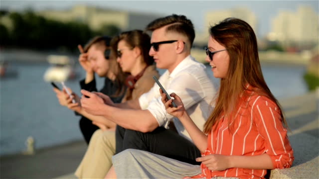 Cuatro-amigos-riendo-felices-y-viendo-las-redes-sociales-en-un-teléfono-inteligente-en-la-calle.-Cada-uno-con-su-propio-teléfono.-Mejores-amigos-y-estudiantes-que-pasan-tiempo-juntos-al-aire-libre