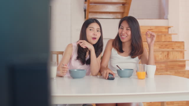 Asiatische-lesbische-Paar-fernsehen,-während-frühstücken-auf-dem-Tisch-in-der-Küche-in-morgendliche-San.