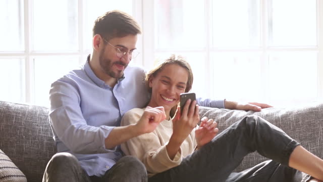 Glückliches-Paar-sprechen-lachen-blick-auf-Smartphone-sitzen-auf-der-Couch