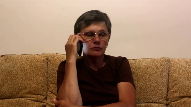 Attraktive-erwachsene-Frau-macht-einen-Anruf-auf-ihrem-Smartphone,-sitzen-auf-einem-Sofa-zu-Hause.