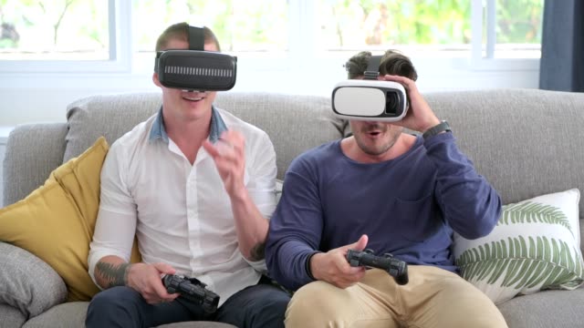Gay-couple-relaxing-on-couch-playing-virtual-reality-games.-Having-fun-competing-game.