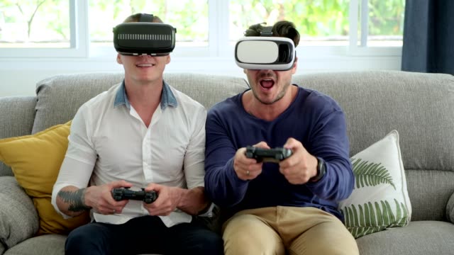 Gay-couple-relaxing-on-couch-playing-virtual-reality-games.-Exciting-mood.