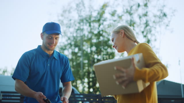 Beautiful-Young-Woman-Meets-Delivery-Man-who-Gives-Her-Cardboard-Box-Package,-She-Signs-Electronic-Signature-POD-Device.-Courier-Delivering-Parcel-in-the-Suburban-Neighborhood