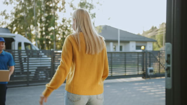 Beautiful-Young-Woman-Holding-Delivered-Cardboard-Box-Package,-She-Signs-Electronic-Signature-POD-Device,-Says-Goodbye-to-Delivery-Man.-Parcel-Delivery-in-Suburban-Neighborhood.-Slow-Motion-Low-Angle
