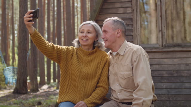 Cónyuges-mayores-haciendo-selfie-cerca-de-House-in-Woods