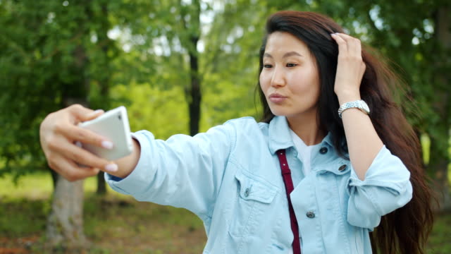 Schöne-asiatische-Dame,-die-Selfie-im-Freien-im-Park-posiert-lächelnde-Holding-Gerät