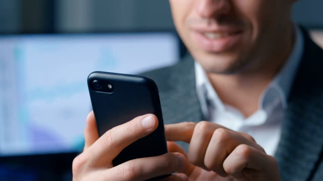 Close-up-of-a-successful-businessman-in-a-suit-is-using-a-smartphone-in-the-office-at-the-workplace.-Man-uses-the-application-on-a-mobile-phone,-office-on-the-background