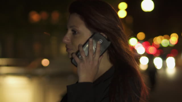 Happy-Attractive-redhead-woman-with-black-jacket-and-red-hair-having-phone-conversation-on-her-smartphone-by-night.-Paris-4K-UHD.-Slow-Motion.