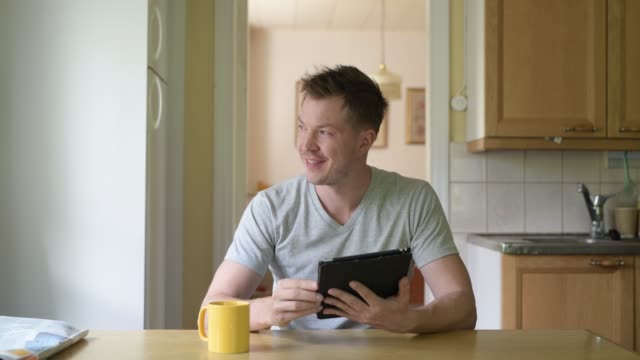 Junger-nachdenklicher-Mann-mit-digitalen-Tablet-sam-es-am-Fenster