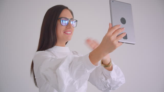 Nahaufnahme-Porträt-der-jungen-hübschen-kaukasischen-Geschäftsfrau-in-Brille-mit-einem-Videoanruf-auf-dem-Tablet-sprechen-fröhlich-im-weißen-Büro-stehend