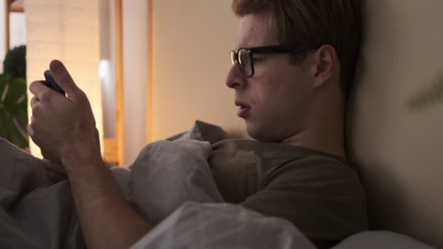 Young-man-using-mobile-phone-in-bed
